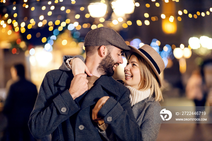 Amorous Christmas couple in love hugging on the street on Christmas. An amorous young couple is standing on the street on Christmas eve, hugging and looking at each other.