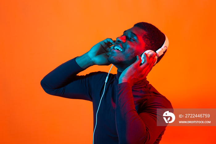 Young african-american man’s listening to music in headphones in neon light. Male portrait. Concept of human emotions, facial expression, holidays or weekend, hobby,