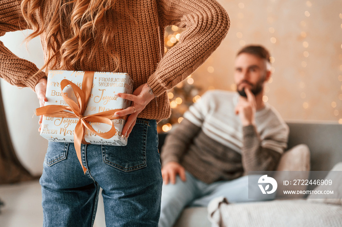 Woman is with gift box for the man. Lovely young couple are celebrating New Year at home