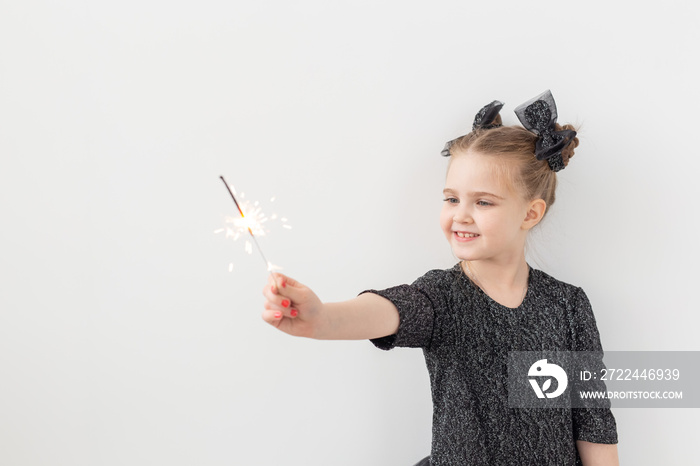 Holidays, christmas and new year concept - Happy child holds burning sparkler in her hand over white background with copy space