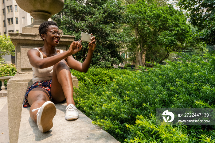 Young woman in tank top holding smart phone outdoors