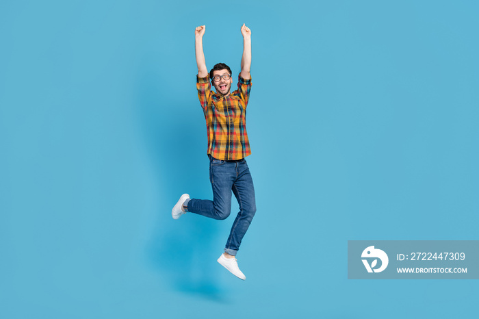 Full size portrait of overjoyed active man raise fists jumping luck isolated on blue color background