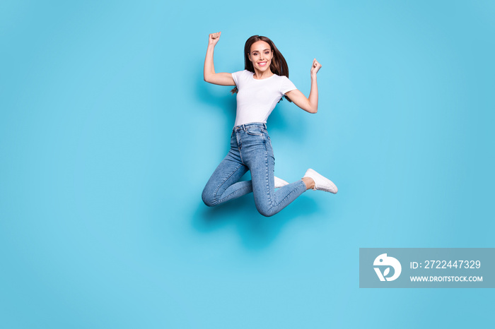 Full size photo of cute lady raising fists looking wearing white t-shirt denim jeans sneakers isolated over blue background