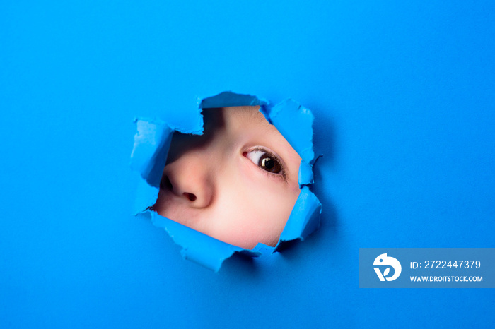 Through paper. Kid looking through paper. Spy eye watching through a hole. Child’s eye looking through hole. Eye through paper. Boy breaks paper.