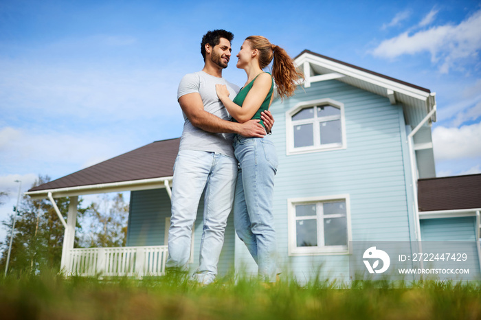 Young amorous couple looking at one another while spending summer day by their new house