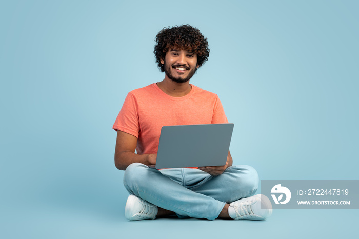 Handsome indian man using modern laptop on blue