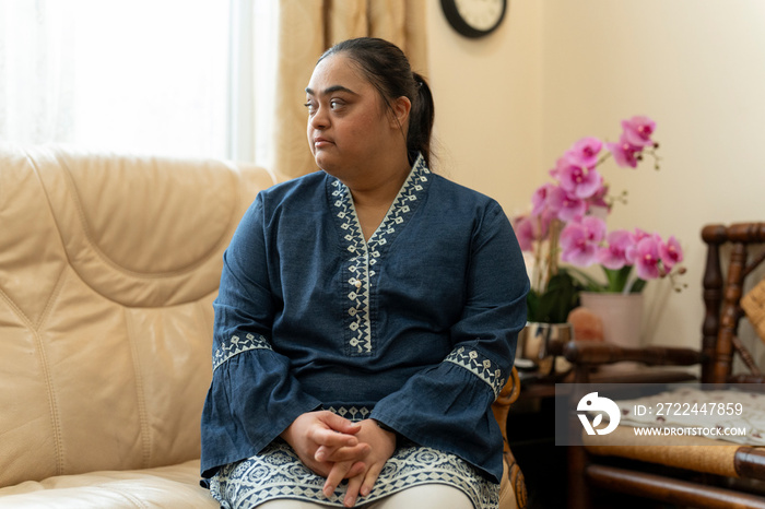 Portrait of young woman with down syndrome sitting on sofa at home