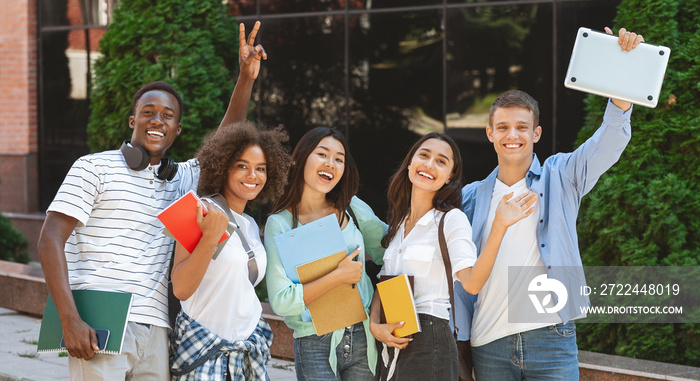 Happy students with workbooks and laptop posing over campus background