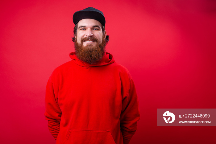 Portrait of handsome bearded guy in red hoody and black hat over isolated wall background