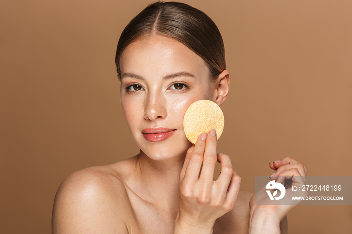 Beautiful concentrated young amazing woman posing isolated over brown chocolate background wall holding makeup remover exfoliate pad.