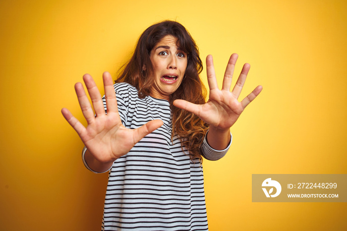 Young beautiful woman wearing stripes t-shirt standing over yelllow isolated background afraid and terrified with fear expression stop gesture with hands, shouting in shock. Panic concept.