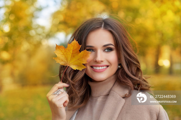 Closeup portrait of a beautiful autumn woman standing near colorful autumn leaves. Pretty happy cheerful model looking at camera.