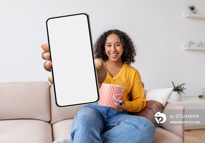 Cheerful Young Black Female Holding Popcorn And Showing Big Blank Smartphone