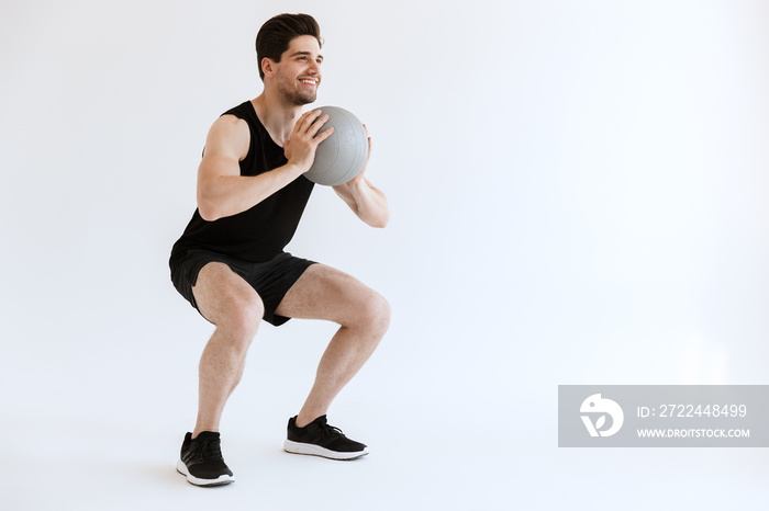 Strong young sports man make squats exercise with ball isolated over white background.