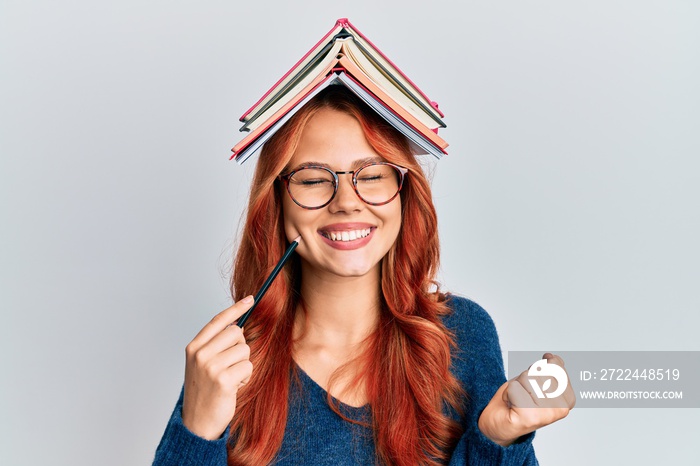 Young redhead woman holding books over head screaming proud, celebrating victory and success very excited with raised arm