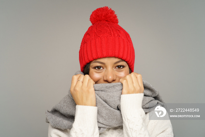 Funny woman in sweater, knitted woolen hat and scarf covering face. Joyful african american female wearing warm clothes for cold weather and frost. Isolated studio portrait of cute cheerful black girl