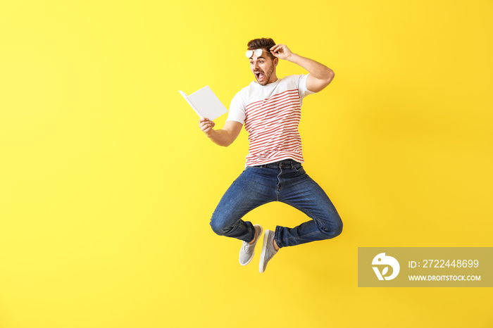 Jumping young man with book on color background