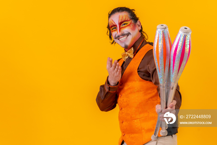 Portrait of a juggler in a vest with a painted face juggling with maces on a yellow background