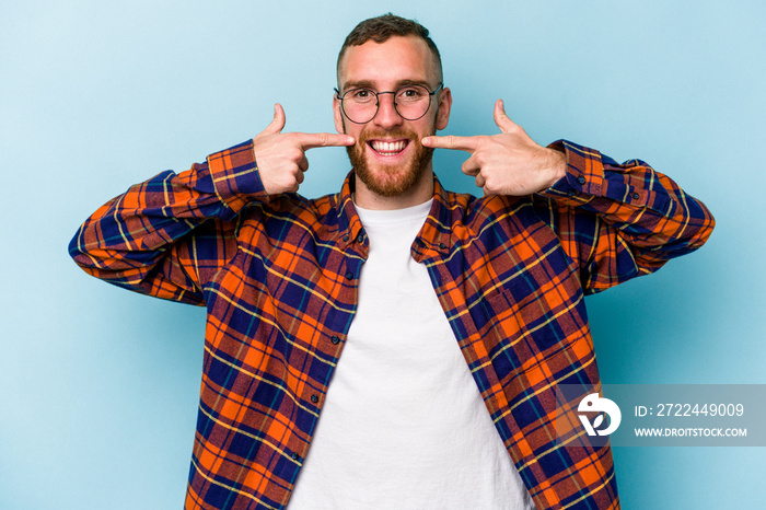 Young caucasian man isolated on blue background smiles, pointing fingers at mouth.