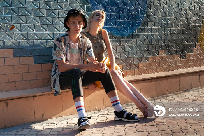 Young guy with a girl stylishly dressed in fashion. Against the background of the wall. The guy in the shirt and t-shirt with a floral print. Sandals with socks.