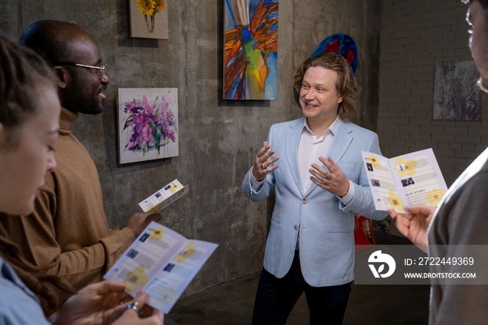 Happy elegant artist interacting with intercultural guests of exhibition of his artworks in gallery