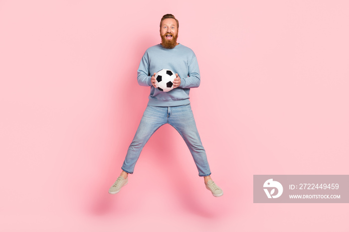 Full size portrait of energetic overjoyed man jumping arms hold football isolated on pink color background