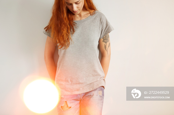 Young girl wearing grey blank t-shirt and blue jeans. Concrete white wall background, flare light