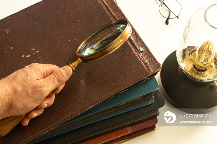 Hand holding a magnifying glass over old photo albums, Luminous vintage lamp, Concept of memories and historical and family research