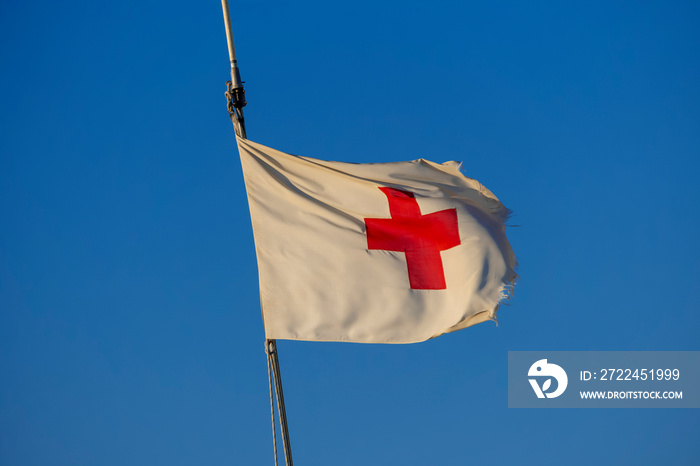 Drapeau de la croix rouge usé par le vent et avec un grand ciel bleu