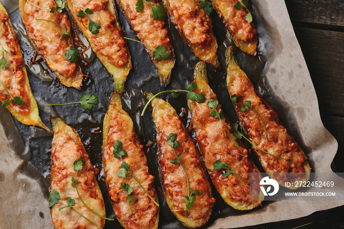 Baked stuffed zucchini boats. Zucchini stuffed with meat, vegetables, cheese and parsley. Healthy food concept. Zucchini boats in a baking tray on table.