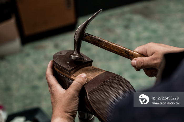 Male cobbler holding shoe and nailing a heel with hummer. Close-up on hands of professional shoemaker.