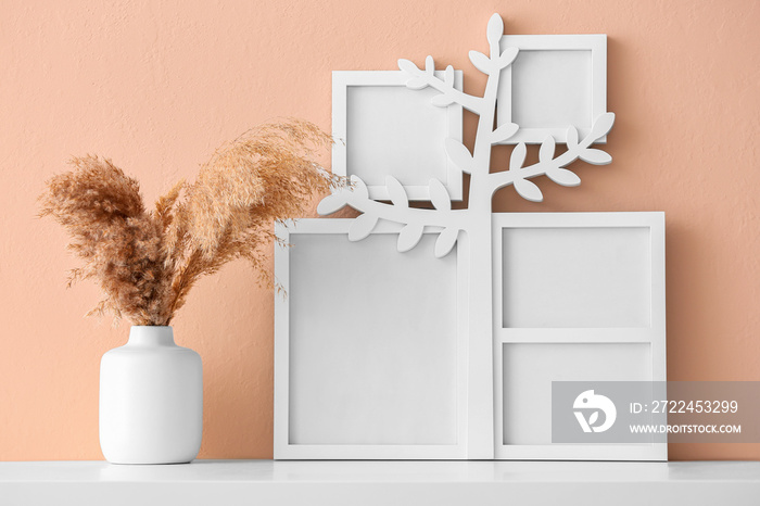 Family tree with photo frames, vase and pampas grass on table near beige wall