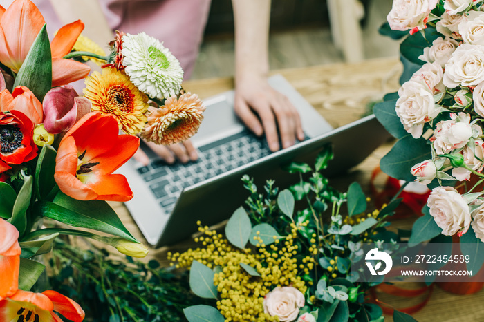 Faceless shot of salesperson using laptop at counter in shop surrounded with flowers.