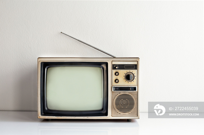 Vintage old television on white table with antenna in front of white wall background, front view, blank screen