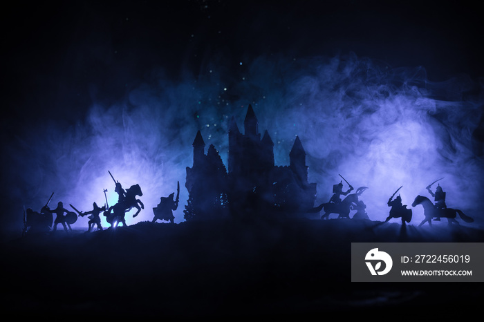 Medieval battle scene with cavalry and infantry. Silhouettes of figures as separate objects, fight between warriors on dark toned foggy background with medieval castle. Night scene. Selective focus