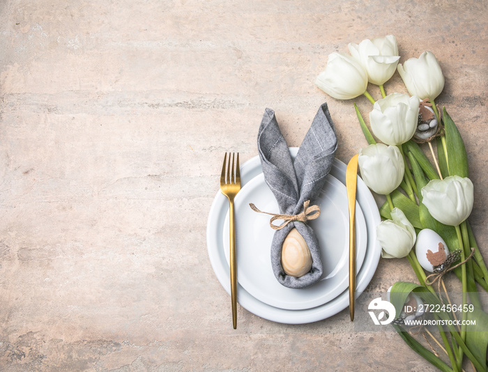 Easter holiday table setting with bunny  from egg on white plate and tulips flowers.  Gray concrete table, top view with copy space for text. Happy Easter background