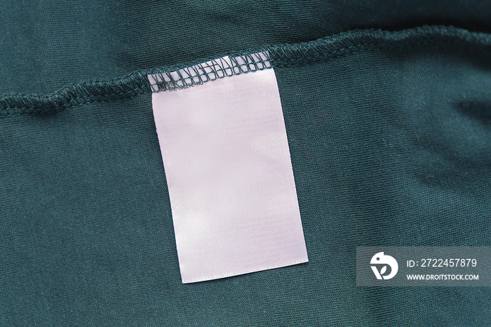 Blank white laundry care clothes label on green fabric texture background.