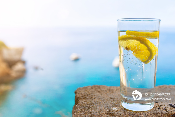 close-up of drinking glass with cold carbonated water or soft drink and lemon slice against blue sea and sky