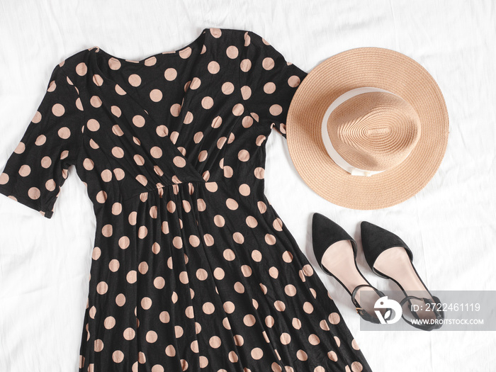 Woman’s feminine outfit with black polka-dot dress, black smart shoes and a rounded hat isolated on white linen background. Flat lay. Top view.