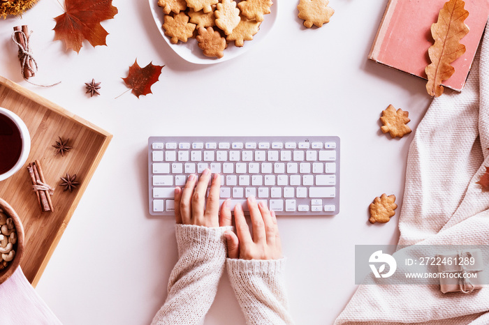 Flat lay and top view of home office desk. Workspace with woman hands, laptop, autumn leaves and flowers, cookies, coffee on cozy background