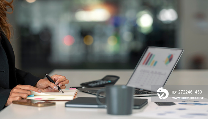 young businesswoman in suit writing business plan and analyzing business growth graph on laptop computer at desk in modern coworking office.