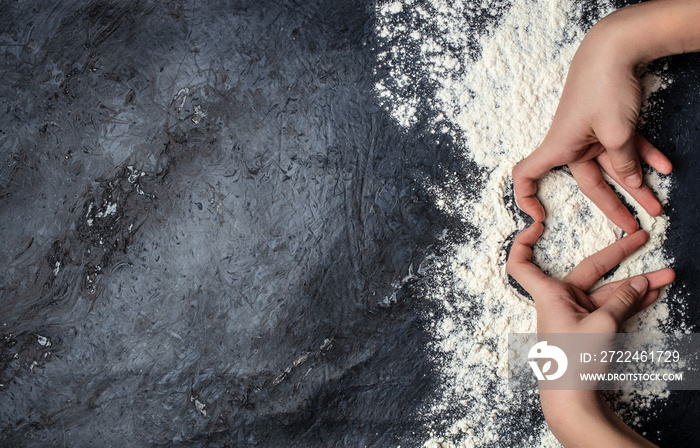 Close-up of hands in flour, making a heart on cooking dark table. banner, menu, recipe place for text, top view