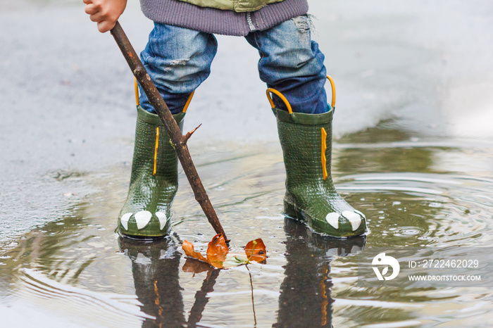 child with rain boots jumps into a puddle