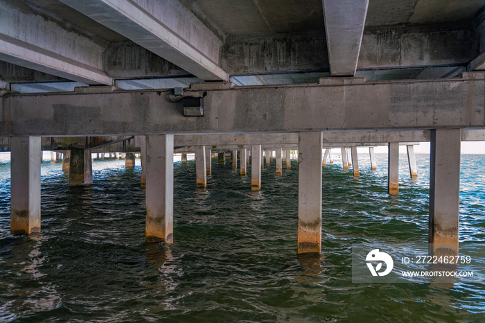 Underneath a concrete bridge over the water at Rickenbacker Causeway in Miami, Florida. Views of bridge support pillars with dried algae marks.