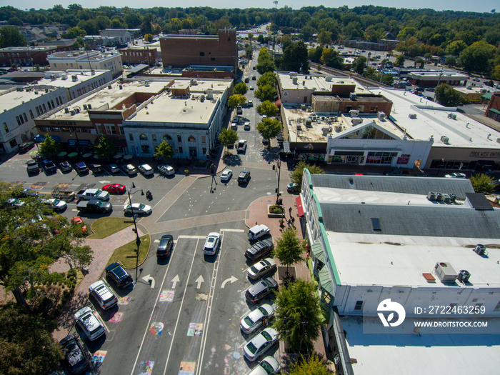 an aerial shot of an intersection with cars driving and cars parked surrounded by buildings and lush green trees in Marietta Georgia USA