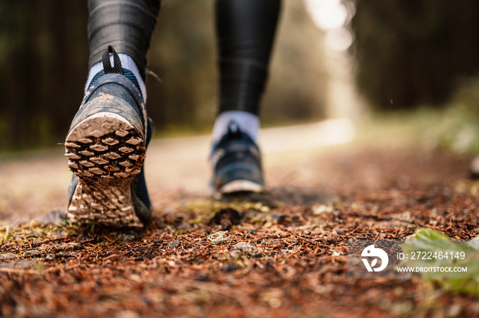 Fit female jogger training for cross country forest trail race in nature park. Detail of running trail shoes.