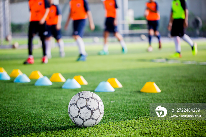 Soccer ball on green artificial turf with blurry of maker cones and player training.