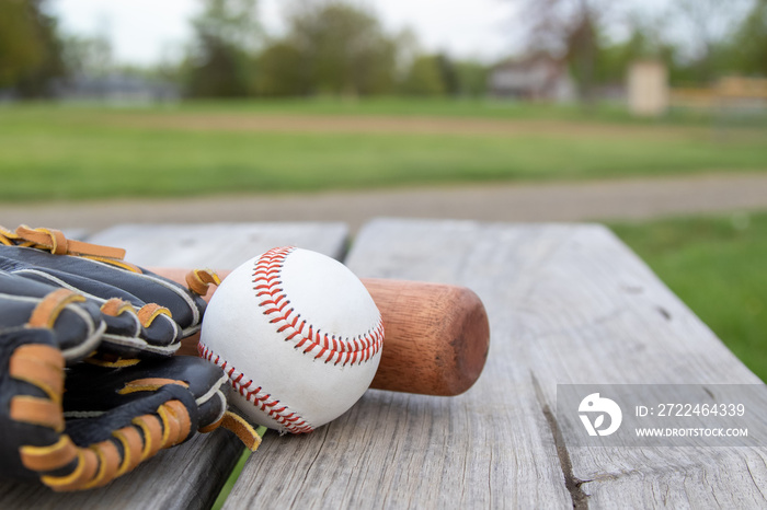 baseball mitt, ball and glove on park pinic table with baseball field in the background room for copy space.