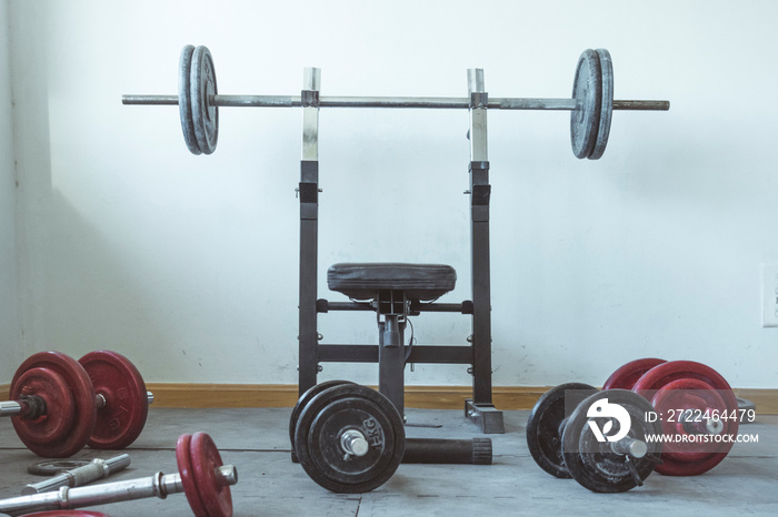 A sunlit weight area of a gym. There is a weight bench that is surrounded by stacks of weights.