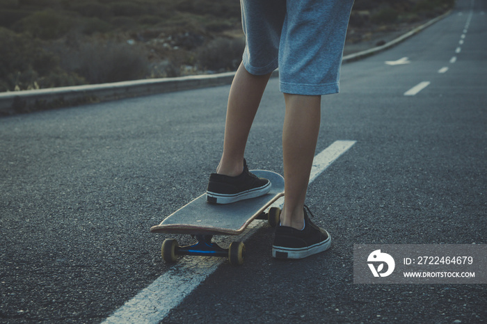 Boy with skateboard is about to start his ride on the road on the center line. Teen skater on a free empty road. Close up of feet of skateboarder on board starting a ride. Foot on deck. Let’s start